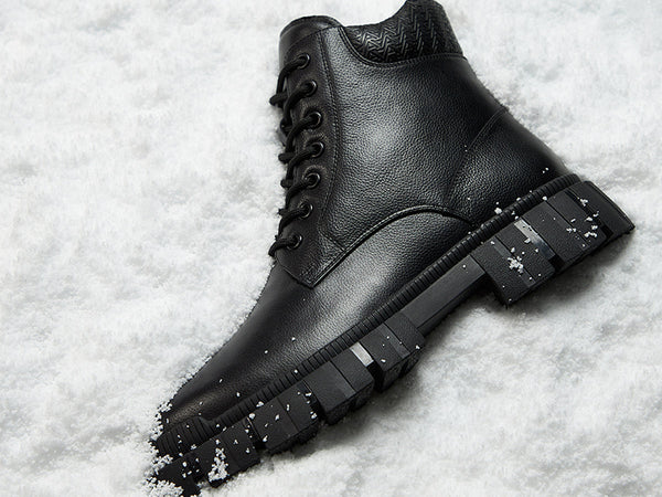 Black leather boot with a thick sole on a snowy background.